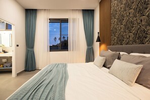 A modern bedroom with a large bed, a nightstand, a lamp, and a view of palm trees through the window.