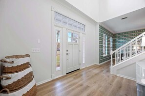Un pasillo con una puerta blanca, una escalera y un papel tapiz decorado.