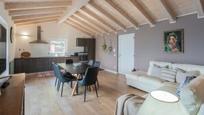 A modern kitchen with dark cabinets, a dining table with chairs, and a white sofa in a living area. - Blooms by the Lake by Rent all Como (Trezzone)