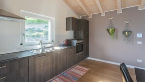 A modern kitchen with dark wood cabinets, stainless steel appliances, and a window providing a view of greenery outside. - Blooms by the Lake by Rent all Como (Trezzone)