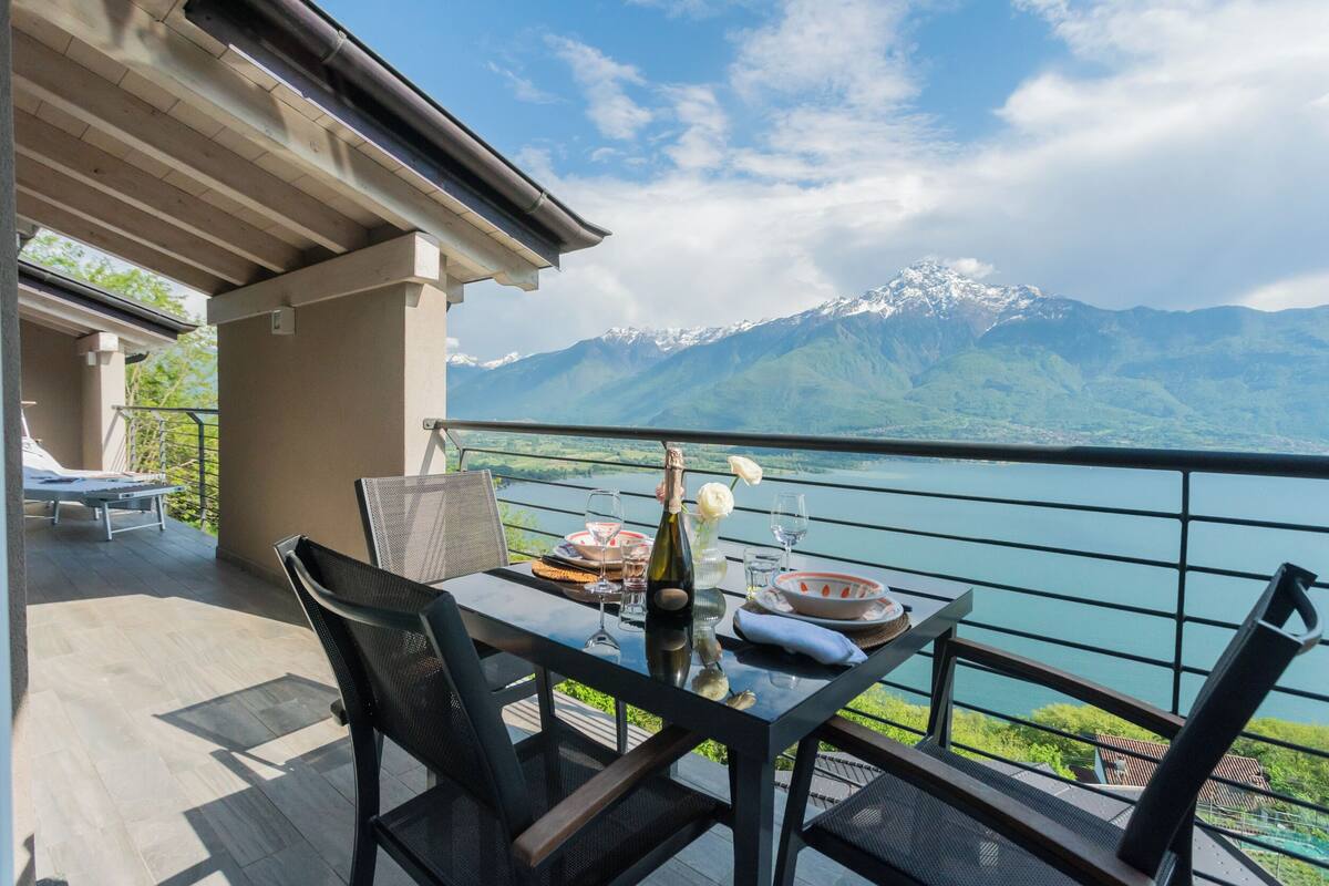 Une terrasse avec une table dressée pour le dîner, offrant une vue sur un lac et des montagnes.