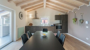 A modern kitchen with a dining area, featuring a large wooden ceiling, dark cabinets, and a central island with a bowl. - Blooms by the Lake by Rent all Como (Trezzone)