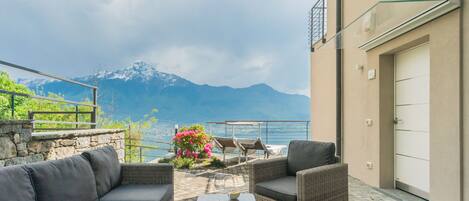 A terrace with wicker furniture, a table with a hat and book, and a view of mountains and water.