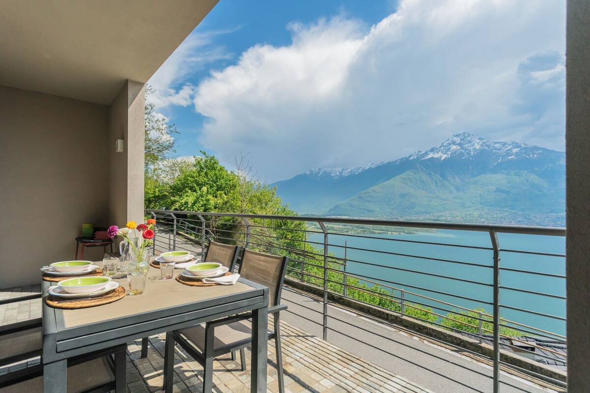 Un balcon avec une table dressée pour le dîner, offrant une vue sur un lac et des montagnes.