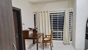 Ein Zimmer mit einem Holztisch, einem Stuhl, einem Fenster mit Vorhängen und einer Tür.