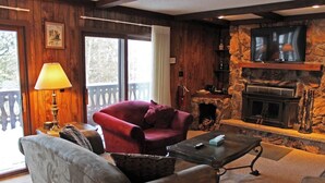 A cozy living room with a stone fireplace, a red armchair, a grey sofa, and a table with a lamp. - A Large Trailside Vacation Home with 2 Large Fireplaces (Ironwood)