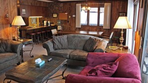 A cozy living room with a stone wall, wooden ceiling, and a bar area with stools. - A Large Trailside Vacation Home with 2 Large Fireplaces (Ironwood)