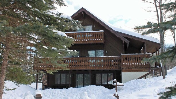 A wooden chalet with a balcony, surrounded by snow and trees. - A Large Trailside Vacation Home with 2 Large Fireplaces (Ironwood)