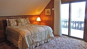 A bedroom with a large bed, a nightstand, a lamp, and a view of a balcony through a sliding door. - A Large Trailside Vacation Home with 2 Large Fireplaces (Ironwood)