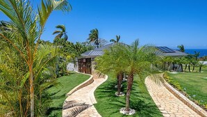 Un resort tropical con un camino de piedra curvo, palmeras y una casa con paneles solares.