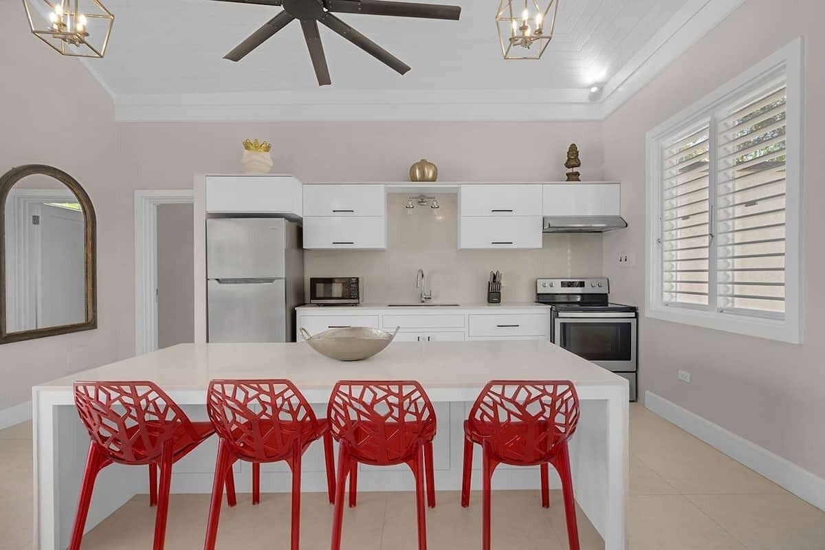 A modern kitchen with white cabinets, a central island with a bowl, and red chairs.