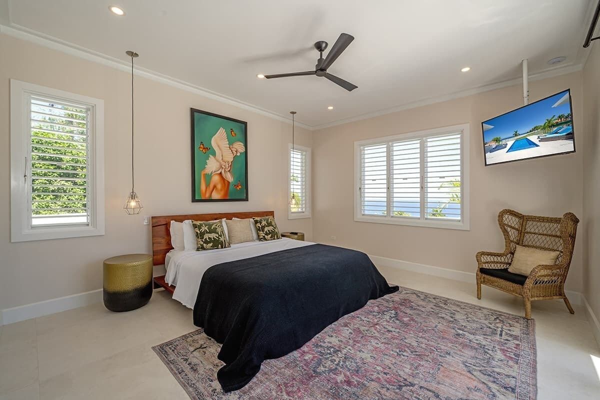 A bedroom with a bed, a ceiling fan, a TV, and a window with blinds.