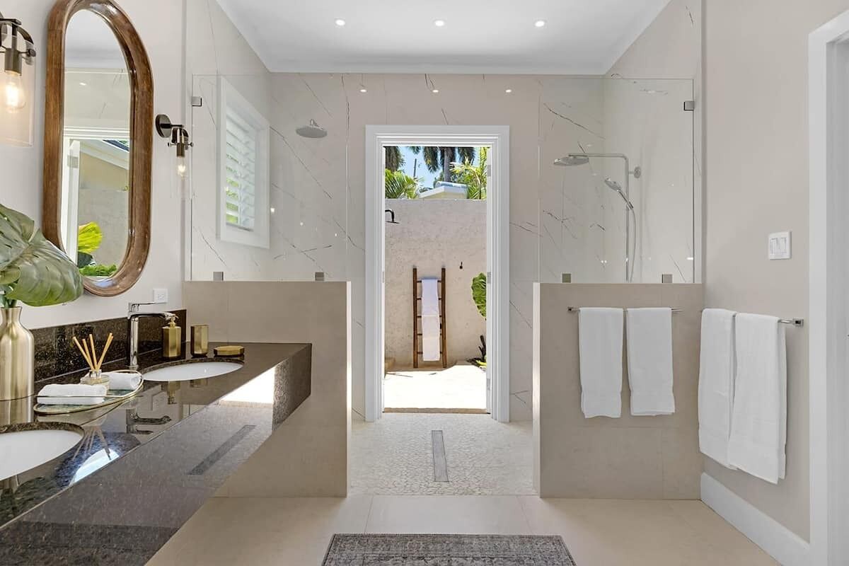 A modern bathroom with a large mirror, two sinks, a shower, and a view of the outdoors.