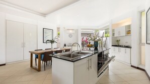 A modern kitchen with white cabinetry, a central island with a sink, and a dining area with a wooden table and chairs.