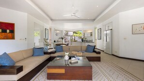 A spacious living room with a modern sofa set, a glass coffee table, and a ceiling fan.