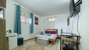 A bedroom with a bed, a desk, a chair, a TV, and a window with curtains. - Nid bleu in Schoelcher: calm, escape, sea view, nature, beaches and amenities (Schoelcher)