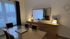 Un comedor moderno con una mesa y sillas de madera, una lámpara colgante, una encimera de cocina con espejo y una ventana con cortinas.