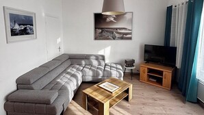 Una sala de estar moderna con un sofá modular, una mesa de centro de madera, un televisor sobre un mueble de madera y una lámpara colgante grande.