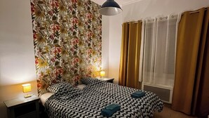 Un dormitorio con cabecera estampada, cama con colcha de motivos geométricos, dos lámparas de noche y una ventana con cortinas.