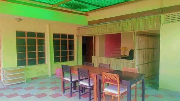 A dining area with a wooden table and chairs, a small kitchen area with a stove, and a window with a view of the outside. - V Food Dormitory (Jodhpur)