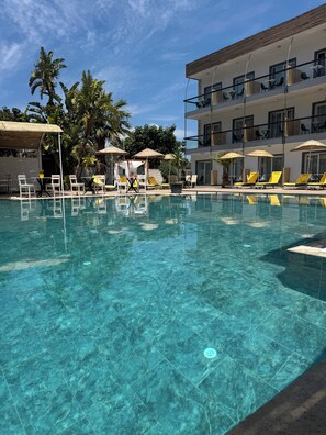 A clear pool with lounge chairs and umbrellas, surrounded by palm trees and a multi-story building. - Mos Hotel Çeşme (Cesme)
