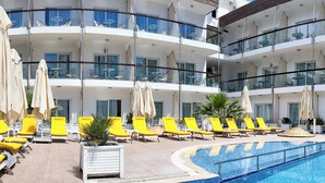 Ett hotell med flera balkonger, en swimmingpool och solstolar.