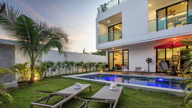 A modern two-story house with a swimming pool, outdoor seating, and a balcony.