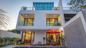 A modern two-story house with a swimming pool, outdoor seating, and a covered patio.