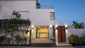 A modern two-story house with a balcony, a front door, and a small staircase leading to the entrance.