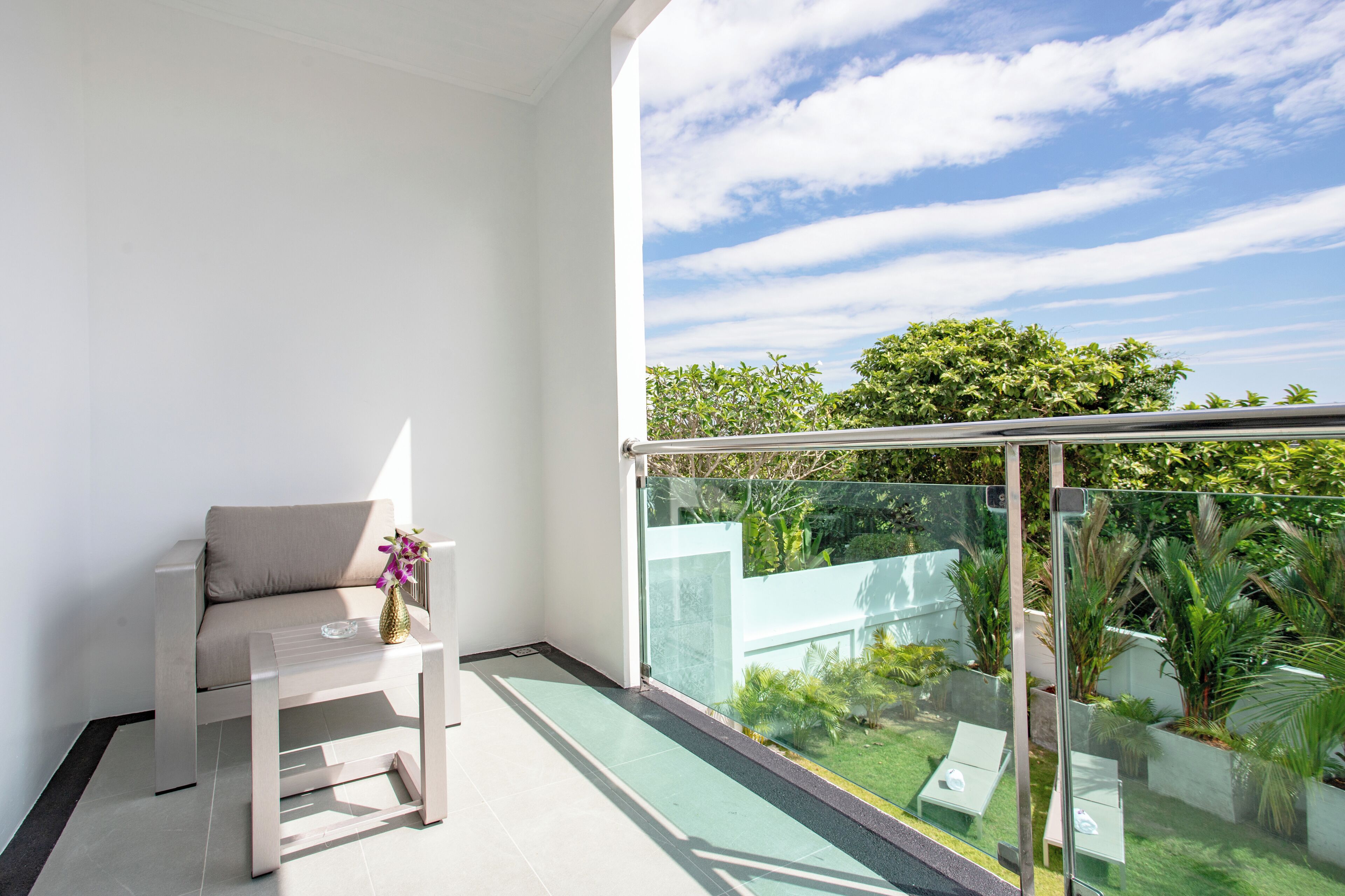 A balcony with a glass railing, a white sofa, and a small table with a vase of flowers.