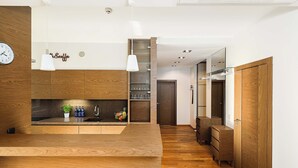 A modern kitchen with wooden cabinetry, a central island, pendant lighting, and a clock on the wall. - Lumina stylish apartment with parking (Lódz)