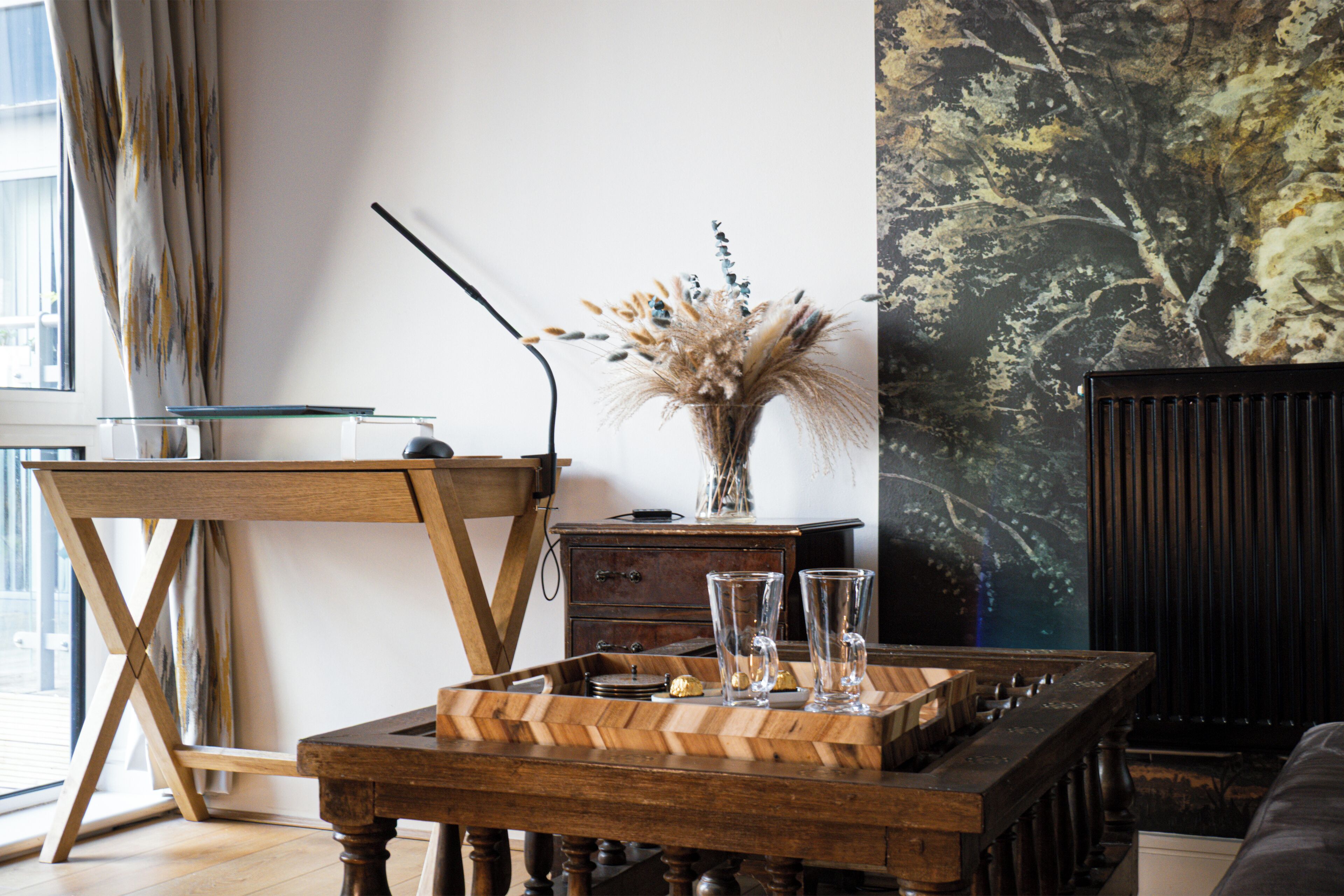 A modern living room with a wooden coffee table, a glass vase with dried flowers, and a painting on the wall.
