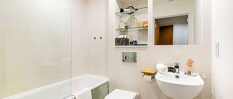 Un baño moderno con ducha de vidrio, inodoro blanco y lavamanos con artículos de aseo.