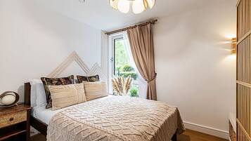 A bedroom with a bed, bedside table, lamp, and curtains.