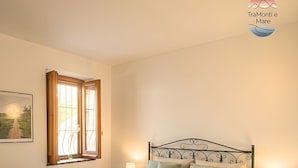 Une chambre à coucher avec un lit en métal, une fenêtre avec des rideaux, une table de chevet avec une lampe et une chaise.