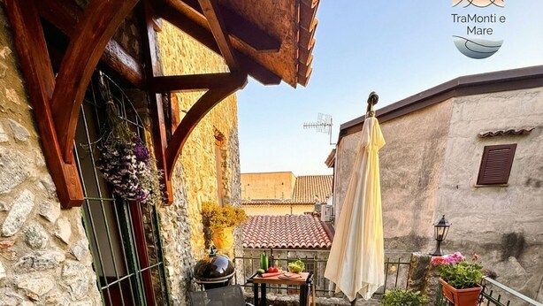 Une terrasse extérieure avec deux chaises longues noires, une petite table ronde sur laquelle se trouve un panier de citrons, et des plantes en pot.