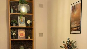 Un coin repas avec une table dressée pour quatre personnes, entourée de chaises jaunes, une bibliothèque contenant divers objets et un tableau accroché au mur.