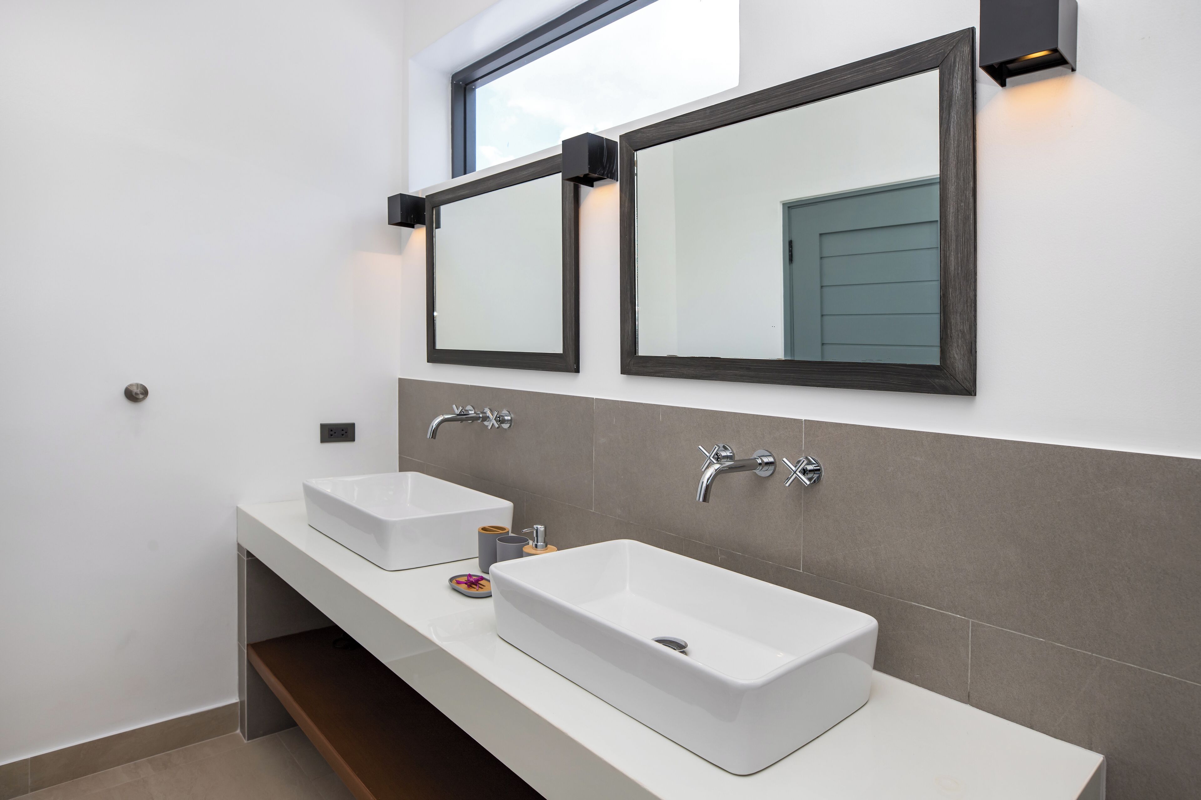 Een moderne badkamer met twee witte wasbakken, een spiegel en een raam erboven.