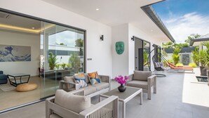 A modern living room with a glass wall, a sofa set, a coffee table, and a decorative mask on the wall. - Luxurious 3 bedrooms pool villa at rawai (Tambon Rawai)