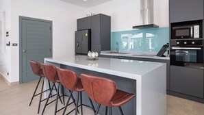 A modern kitchen with a central island, bar stools, a built-in oven, and a microwave. - Luxurious 3 bedrooms pool villa at rawai (Tambon Rawai)
