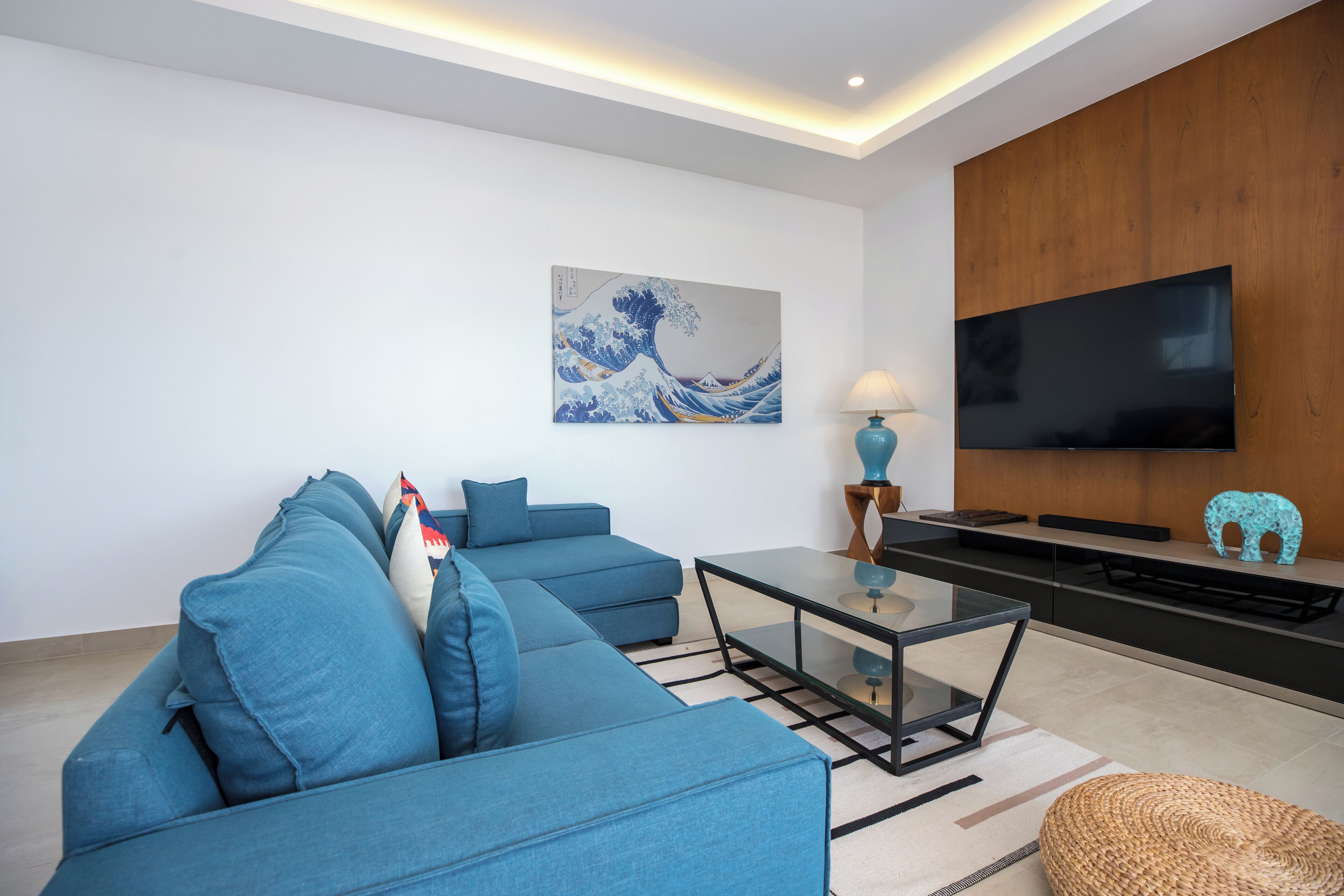 A modern living room with a sectional sofa, a glass coffee table, a flat-screen TV, and a wooden accent wall.