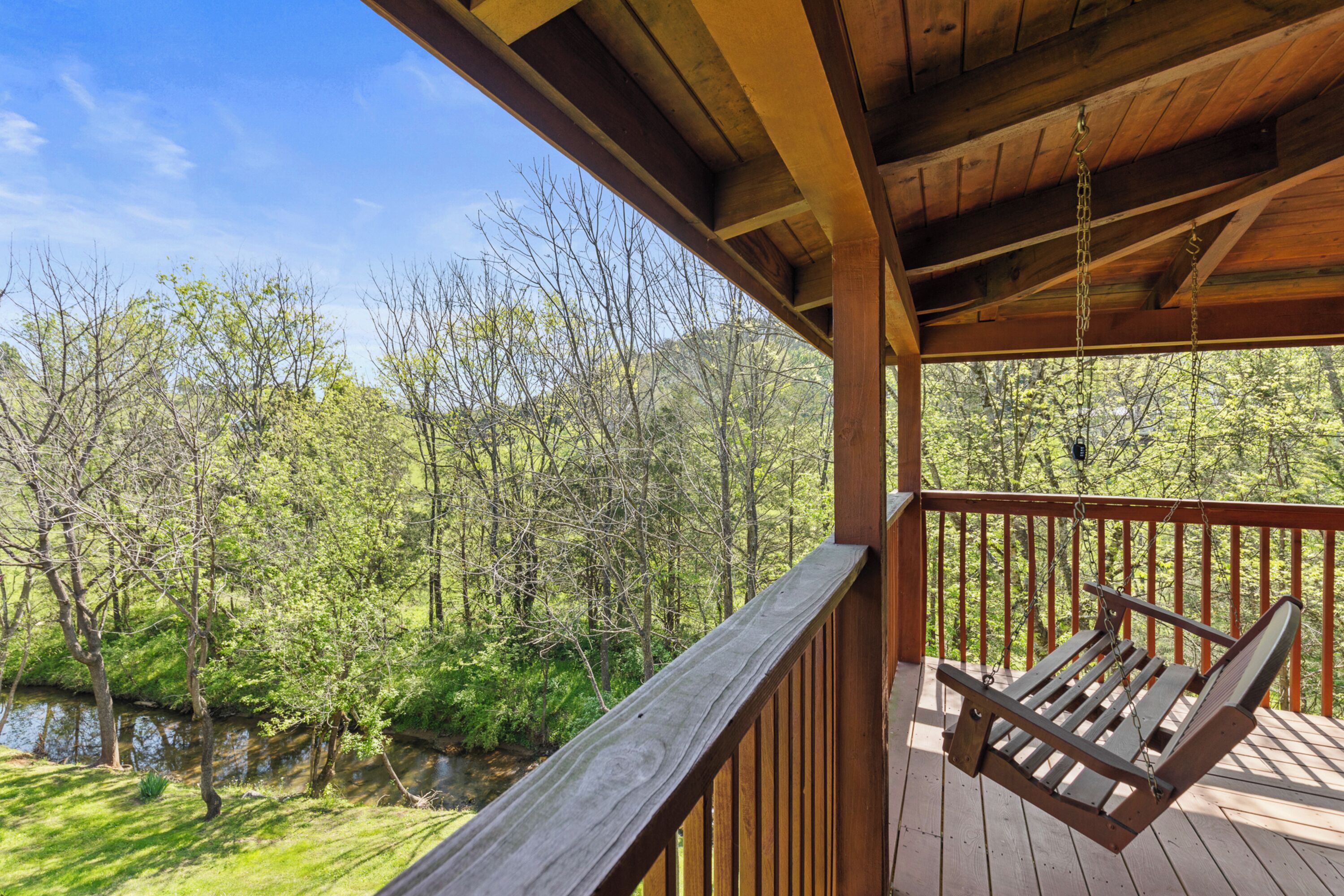 Une terrasse en bois avec une balançoire suspendue, donnant sur une rivière et une zone boisée.