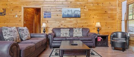 A cozy log cabin interior with two leather sofas, a wooden coffee table, and a fireplace.