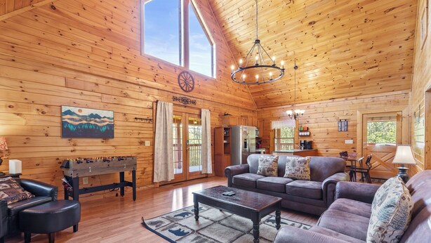 A spacious living room with wooden walls and a high ceiling, featuring a sofa set, a coffee table, and a foosball table. - Serene Creek Cabin (Sevierville)