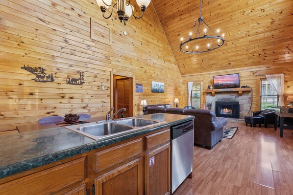A wooden cabin interior with a kitchen, dining area, and living room. - Serene Creek Cabin (Sevierville)