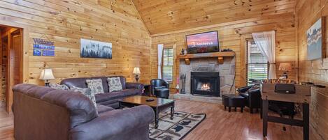 A cozy log cabin interior with a fireplace, a television, a sofa, and a coffee table.