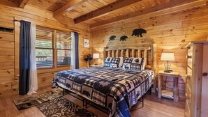 A wooden cabin bedroom with a large bed, a headboard with animal silhouettes, a nightstand, and a lamp. - Serene Creek Cabin (Sevierville)