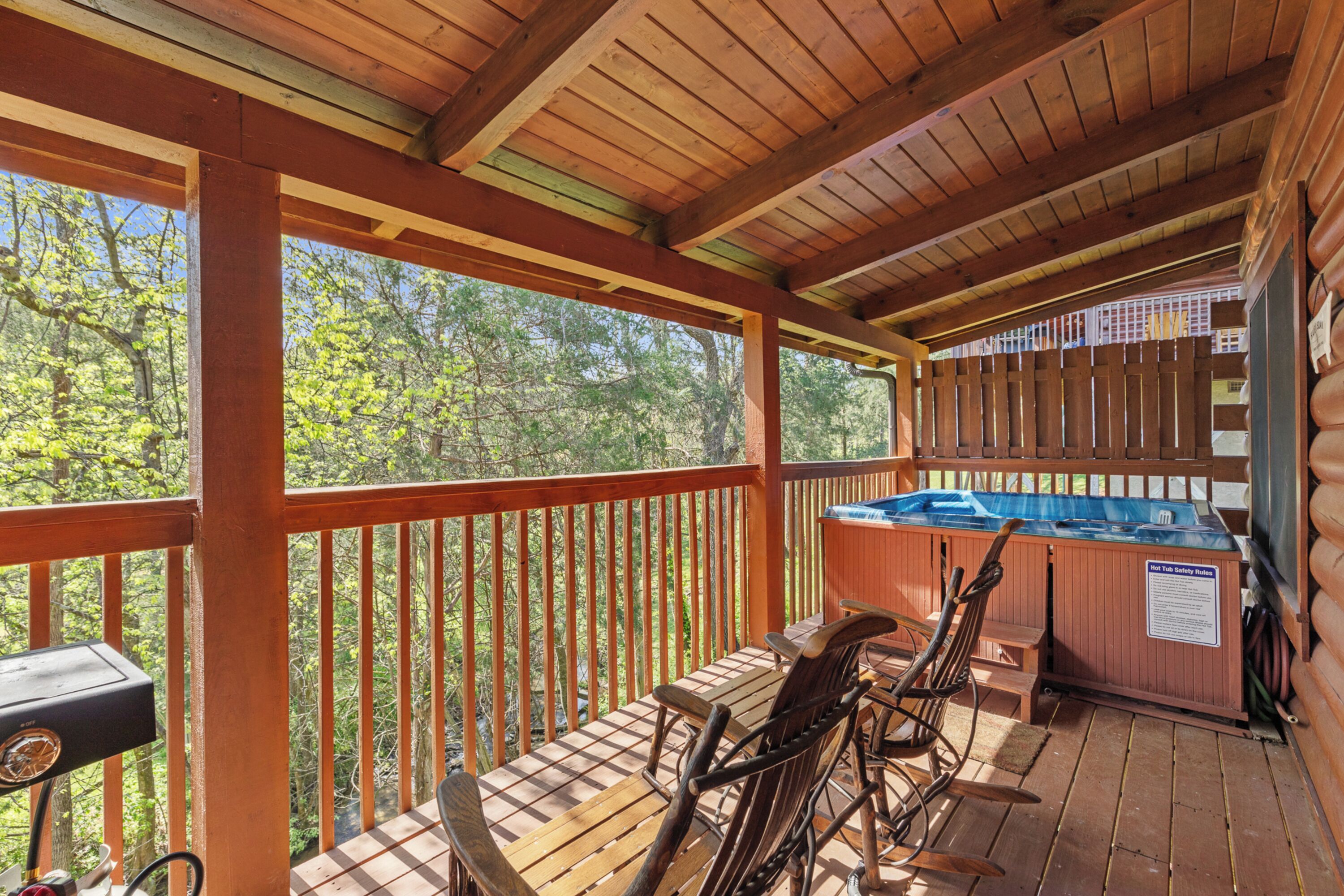 Una terraza de madera con un jacuzzi, sillas de madera y una parrilla.
