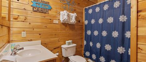 A wooden cabin bathroom with a sink, toilet, and shower curtain.