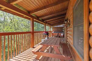 Une terrasse en bois avec des tables de pique-nique et un barbecue, donnant sur une zone boisée.